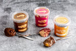 Trio of Roar low saturated fat protein desserts displayed on a mottled grey background with a spoonful of each beside on their spoons