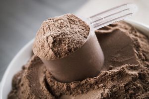 Chocolate whey protein powder in a scoop resting on top of a pot of the same